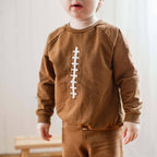 Child wearing a brown football outfit with a white design on a plain background