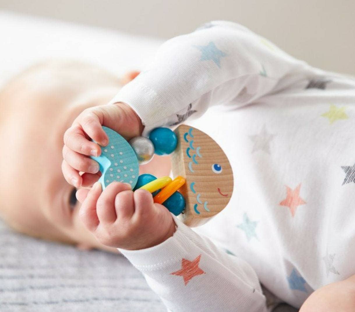 Baby holding a Rattlefish Wooden Baby Rattle with soothing blue and natural wood tones, designed for sensory play and safe for newborns.