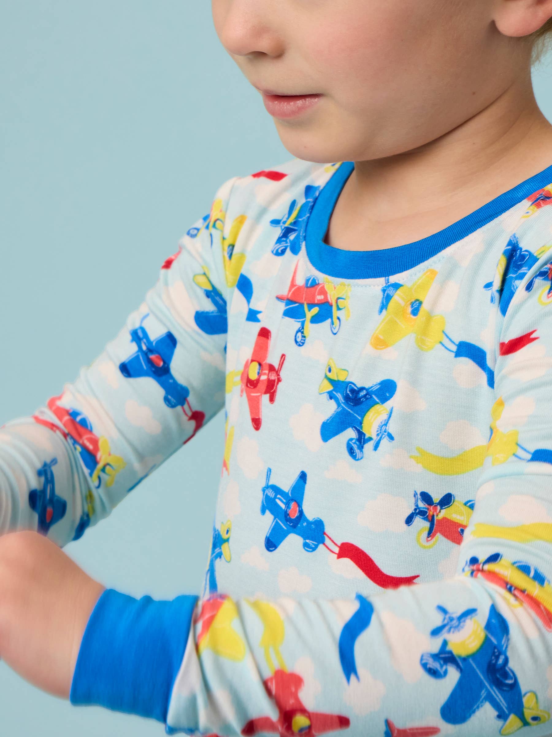Close-up of a child wearing the RuffleButts + RuggedButts - SoftSnooze™ Kids Bamboo Viscose Plane Parade Long Sleeve Pajama Set featuring colorful airplanes on a soft, breathable fabric, perfect for cozy nights and stylish comfort.