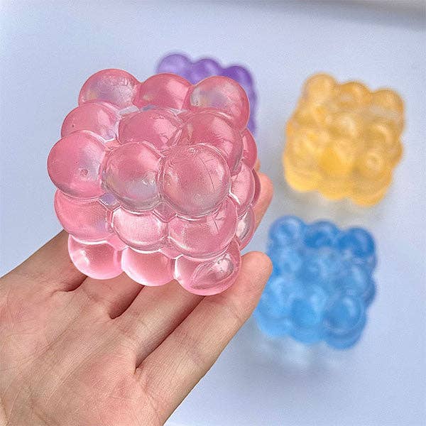 Pink gelatinous ball held in a hand with other colored balls in the background.