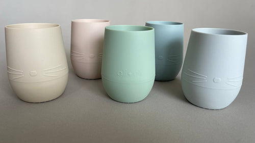 Set of five pastel-colored Ali+Oli - Bunny Face Silicone Open Cup for Baby & Toddler, featuring soft neutral tones and playful bunny face design, perfect for stylish kids accessories.