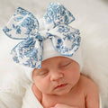 Sleeping newborn wearing ilybean - Blue Toile Floral Bow White Hospital Hat: Blue Floral Bow, a soft white hat with a large blue floral patterned bow, showcasing cozy baby essentials for modern families.