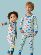 Two young children wearing RuffleButts + RuggedButts - SoftSnooze™ Kids Bamboo Viscose Plane Parade Long Sleeve Pajama Set featuring colorful airplane prints, standing against a light blue background in cozy, stylish sleepwear from a curated children’s boutique.