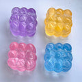 Four translucent bubble-shaped gel cubes in purple, yellow, pink, and blue, arranged in a 2x2 grid on a light gray background.