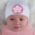 Baby wearing ilybean - Little Sister Hospital Hat White with Pink Flower Patch, wrapped in soft pink knit blanket, cozy newborn essentials from curated children’s boutique.