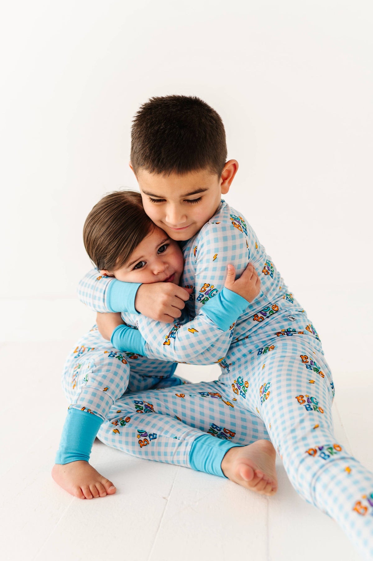Two children in matching pajamas hugging on a white background