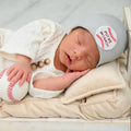 Newborn baby peacefully sleeping in a cozy knit outfit, holding a soft baseball and wearing the ilybean - Put Me In Coach Baby Baseball Hat Newborn Baby Hospital Hat : Gray, styled for modern baby essentials.