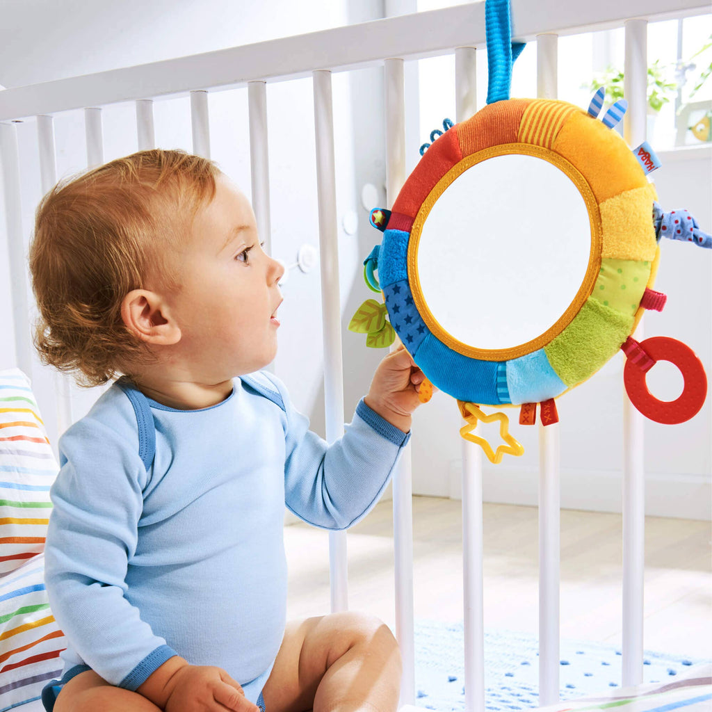 Baby playing with a colorful sensory toy featuring the Rainbow Discovery Mirror, designed for imaginative play and stylish kids clothing essentials in a cozy nursery setting.