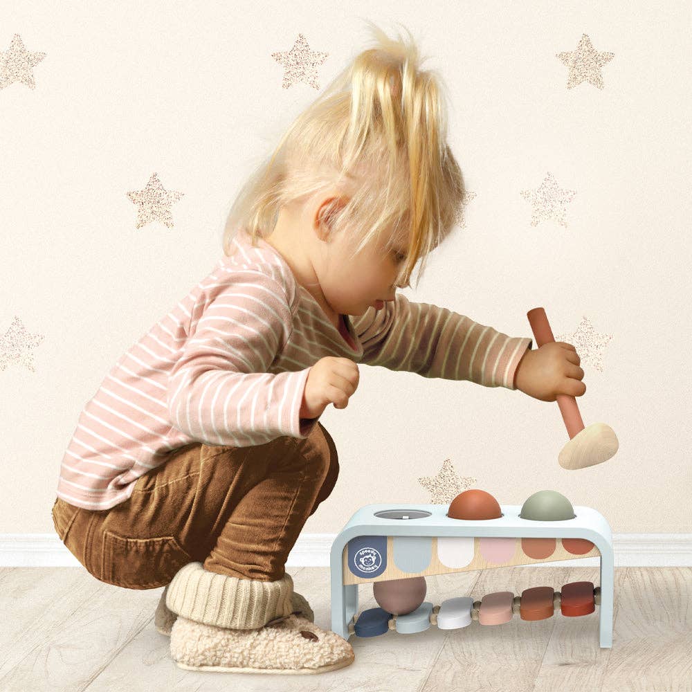 Child playing with the Speedy Monkey - Xylo Bench wooden musical toy, featuring soft neutral colors, promoting imaginative play in a cozy children’s boutique setting.
