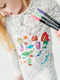 Child wearing Bee Colorful Co. - Mermaid Coloring Pajamas 2 piece set made from Bamboo, partially colored with sea creatures and mermaid designs, holding markers.