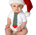 Baby wearing a white onesie and a Santa hat, holding the Tasty Tie® - Tasty Tie Teether, Crinkle Toy, Baby Boy Gift: Santa with a green Santa pattern and red teether tip, perfect for baby shower gifts and cozy baby essentials.