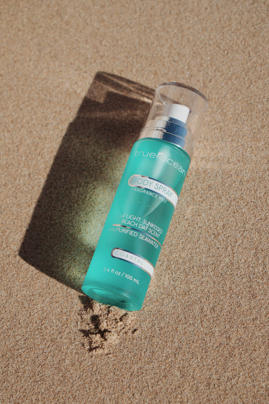 True Ocean - True Ocean: Body Spray - 3.4oz. bottle with a fresh turquoise design lying on sandy beach, evoking a light, sun-kissed coastal scent.