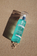 True Ocean - True Ocean: Body Spray - 3.4oz. bottle with a fresh turquoise design lying on sandy beach, evoking a light, sun-kissed coastal scent.