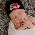 Sleeping newborn wrapped in a soft white blanket wearing an ilybean - Mama's Boy Tattoo Hospital Hat - Black, featuring a heart design and cozy baby essentials from a curated children’s boutique.