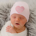 Newborn baby peacefully sleeping while wearing the ilybean - Little SIS Pink Hospital Hat with Pink Heart Patch, a cozy and stylish baby accessory from a curated children’s boutique.