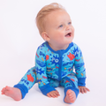 Baby wearing Kiki + Lulu - Kiki + Lulu x Rydel SUPER Convertible Footies, featuring vibrant superhero-themed blue fabric, perfect for cozy baby essentials and stylish kids clothing.
