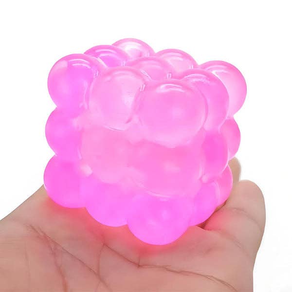 A translucent pink stress toy made of connected bubble-like spheres, being held in a person's hand against a plain white background.