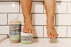 Child’s feet above white tiled bath floor with California Baby - Eczema Cream + Wash Bundle products placed nearby, highlighting cozy baby essentials for sensitive skin care.