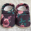 Soft fabric baby shoes with a dark floral pattern featuring pink and green leaves, designed for comfort and style from CLAMFEET - Harlowe, perfect for cozy baby essentials.