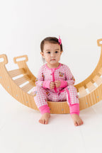 Child wearing pink and white checkered outfit with matching shoes, sitting on a wooden climbing toy.