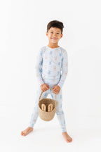 Young child wearing Kiki + Lulu - Peeps + Sleeps Kids Pajamas holding a woven basket with wooden toys, showcasing soft, breathable fabric in playful bunny print pajamas from a curated children’s boutique.