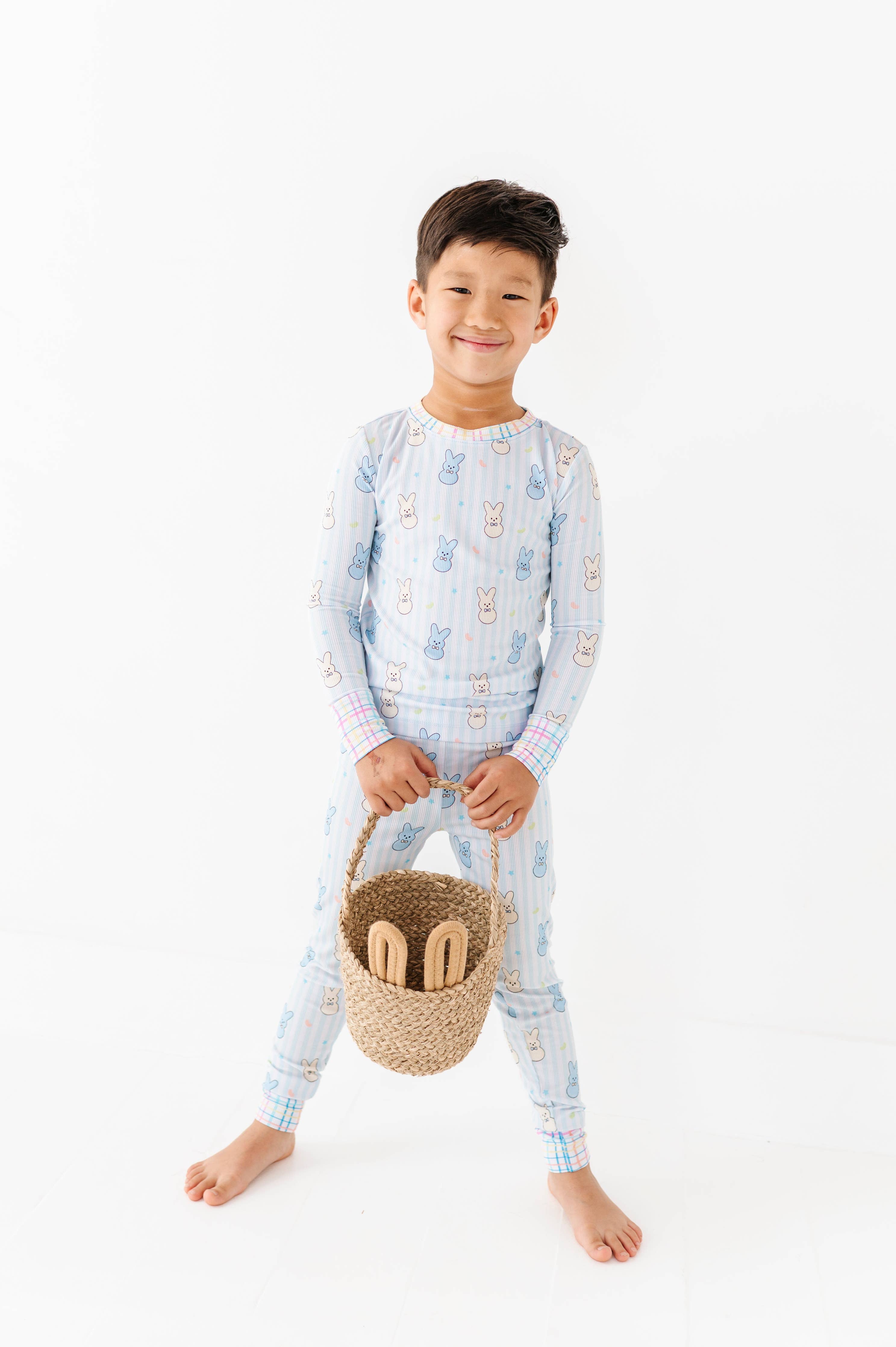 Young child wearing Kiki + Lulu - Peeps + Sleeps Kids Pajamas holding a woven basket with wooden toys, showcasing soft, breathable fabric in playful bunny print pajamas from a curated children’s boutique.