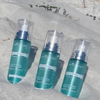 Three bottles of True Ocean - True Ocean: Body Spray - 3.4oz. with teal packaging and clear caps arranged on white sand, evoking a fresh, beachy vibe.