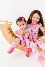 Two children in pink pajamas sitting on a wooden slide.