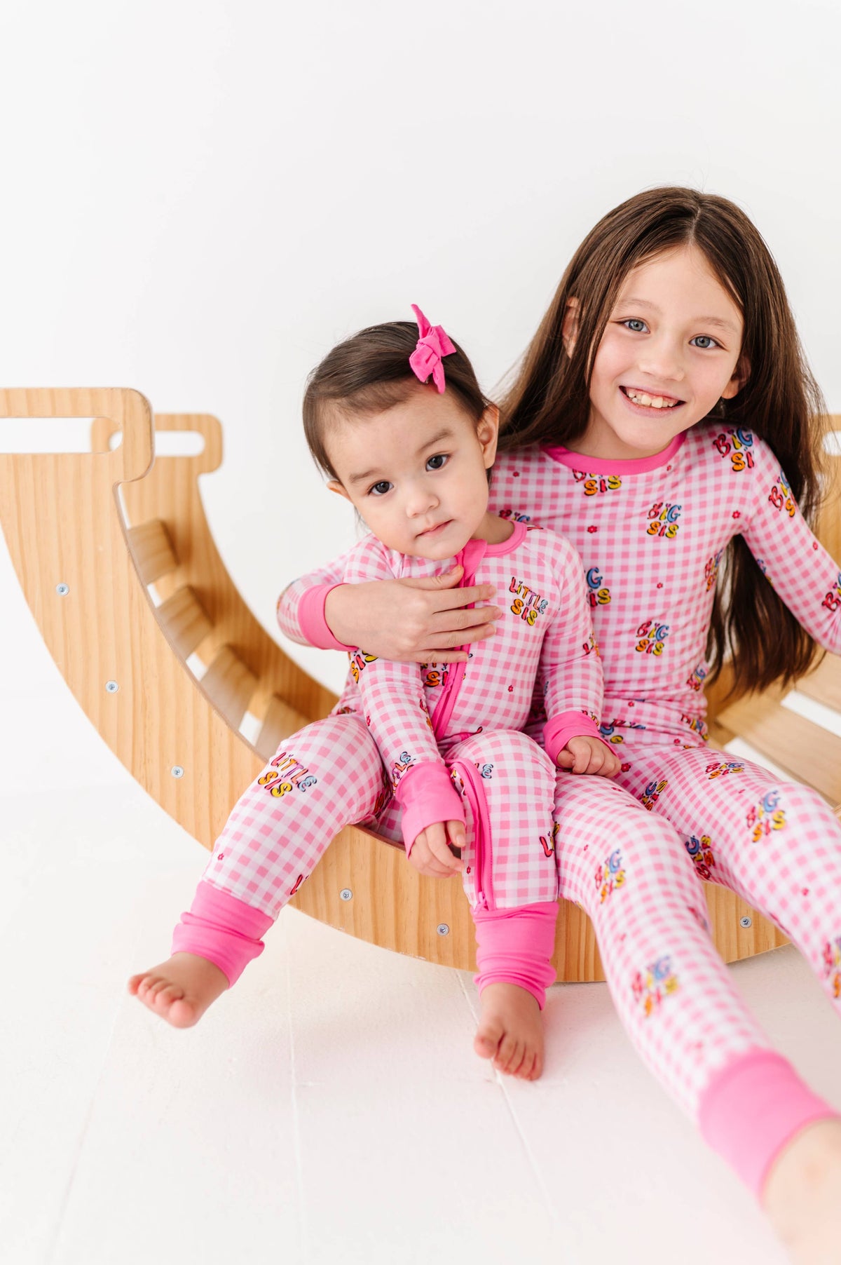 Two children in pink pajamas sitting on a wooden slide.