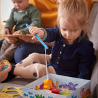 Young child engaged in imaginative play with My Very First Games - Here, Fishy, Fishy! Magnetic Game, promoting sensory learning and fine motor skills in a cozy children’s boutique setting.
