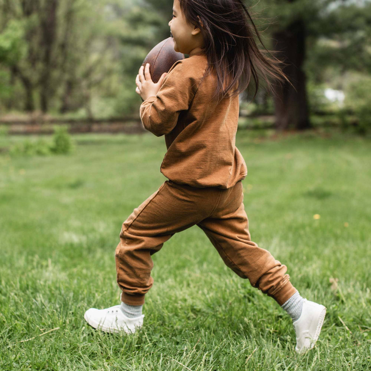 Child in brown football outfit holding a football on grass.