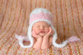Newborn sleeping peacefully wearing The Daisy Baby LLC - Cream Princess Crocheted Handmade Heirloom Baby Gift Hat in soft cream and pink on cozy textured blanket, perfect baby boutique gift.