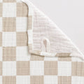 Close-up of soft, neutral beige and white checkered fabric with a corner folded over, featuring a small loop detail from the Itzy Ritzy - Breastfeeding Boss™: Toast Checkerboard, a cozy baby essential perfect for moms and little ones.