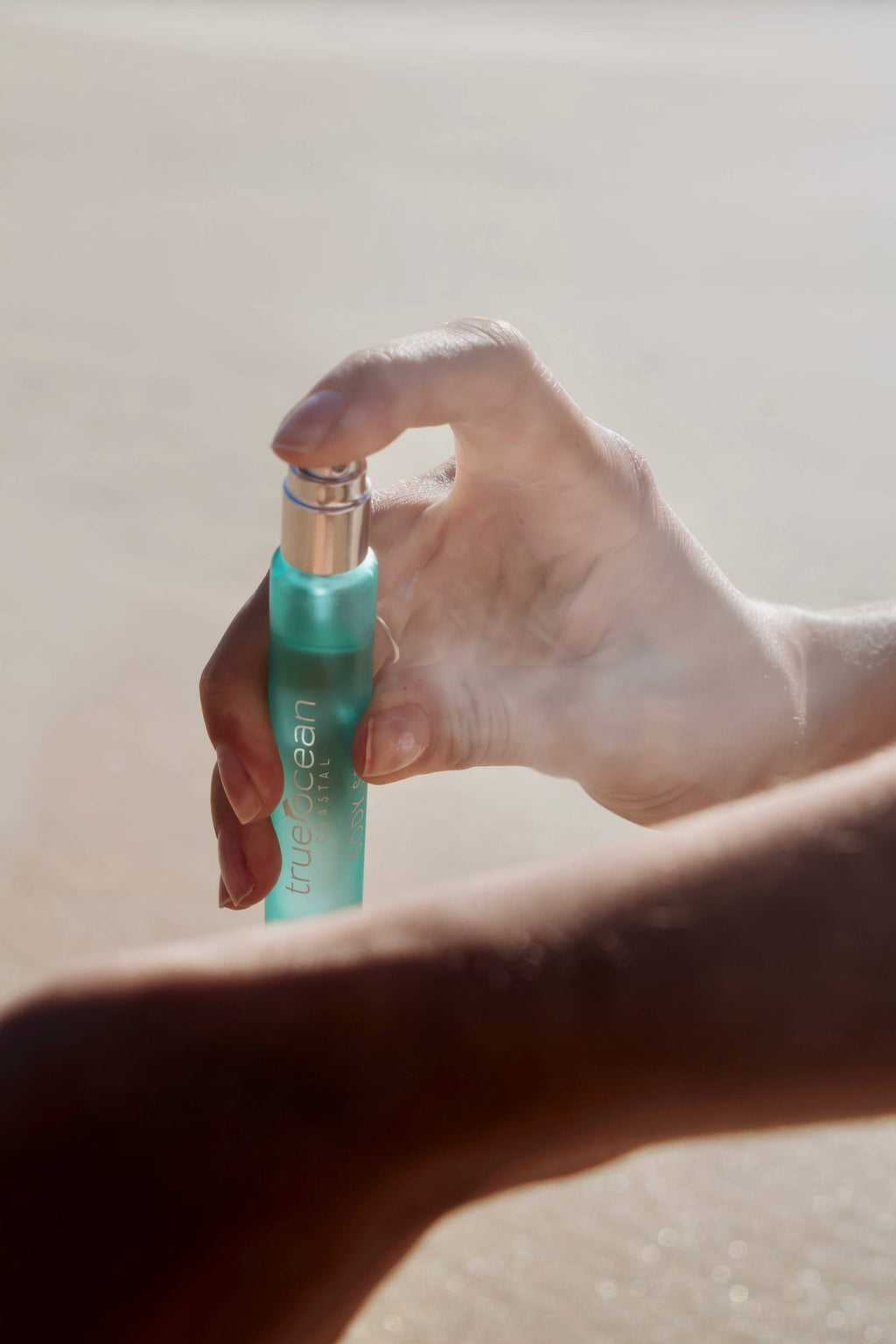 Hand holding and spraying True Ocean - True Ocean Body Spray - Pocket Size with a light mist, set against a soft, neutral background reflecting a calming coastal vibe.