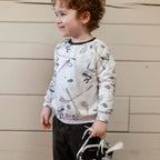 Toddler wearing Burt's Bees Baby - Hockey Season Sweatshirt & Pants Set with hockey-themed print, holding a pair of ice skates, styled in soft neutral colors perfect for modern baby boutique collections.