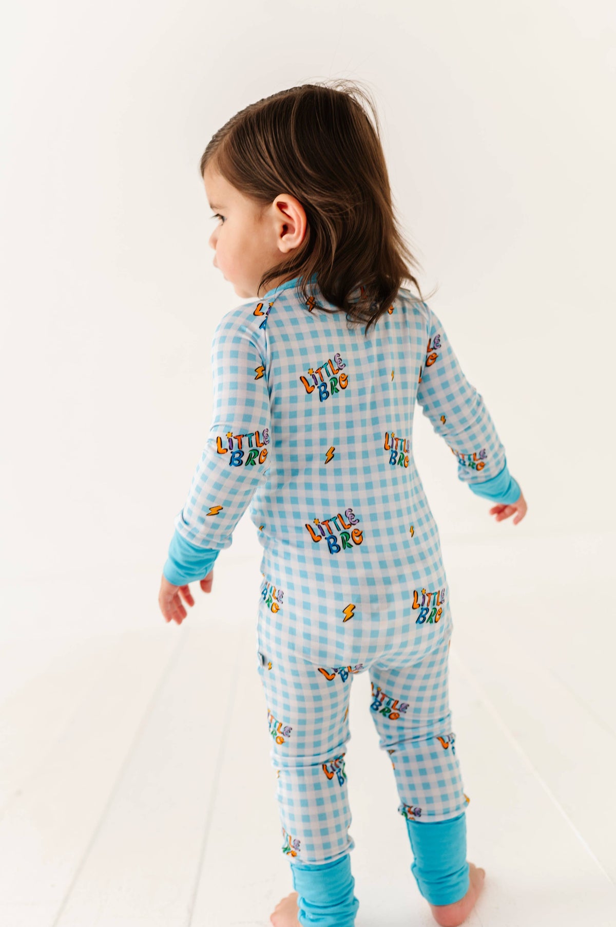 Child wearing a blue checkered onesie with 'Little Bro' text on a white background