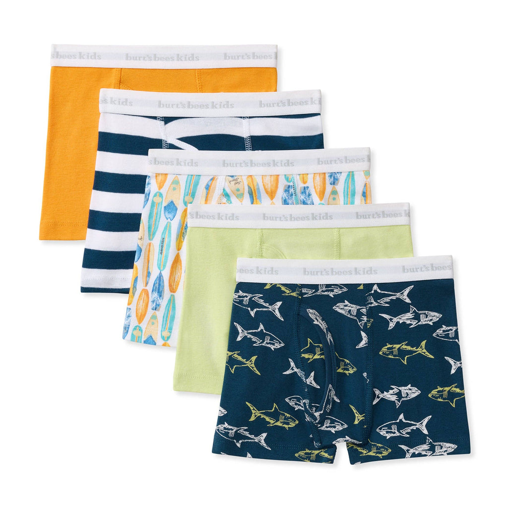A 5-pack of children's boxer briefs, displayed in a staggered fan layout. The set includes solid orange, navy and white stripes, a surfboard pattern, and a light green pair, with the front pair featuring a navy blue shark print.