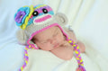 Newborn baby peacefully sleeping wearing The Daisy Baby LLC - Pastel Sock Monkey Crocheted Handmade Heirloom Gift Hat in soft pastel colors, styled with cozy baby essentials from a curated children’s boutique.