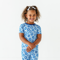 Young girl smiling in blue patterned pajamas featuring circular designs, wearing Kiki + Lulu - Mamma Mia! Here, I Go Again Toddler/Big Kid Pajamas- Short Sleeve and Shorts, styled for cozy comfort and playful mornings.