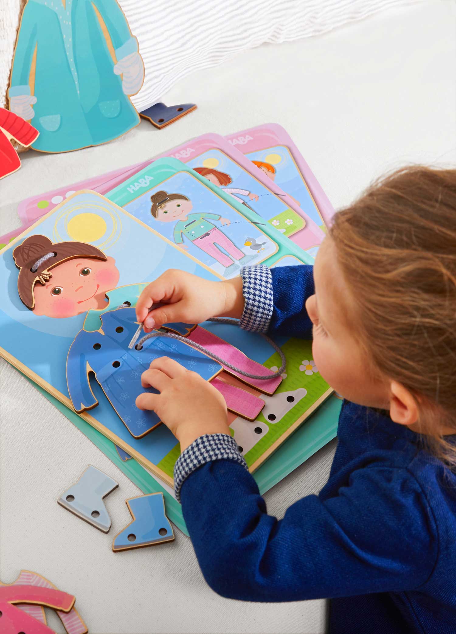 Child playing with the Dress Me Threading & Lacing Game, threading a string through dress pieces on a wooden figure, encouraging fine motor skills and imaginative play.