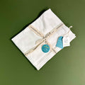 Viverano Organics - Dove White Baby Blanket Sweater Knit (Organic Cotton): Dove White folded on a green surface, tied with a branded ribbon, highlighting soft, organic, breathable baby blanket from a curated children’s boutique.