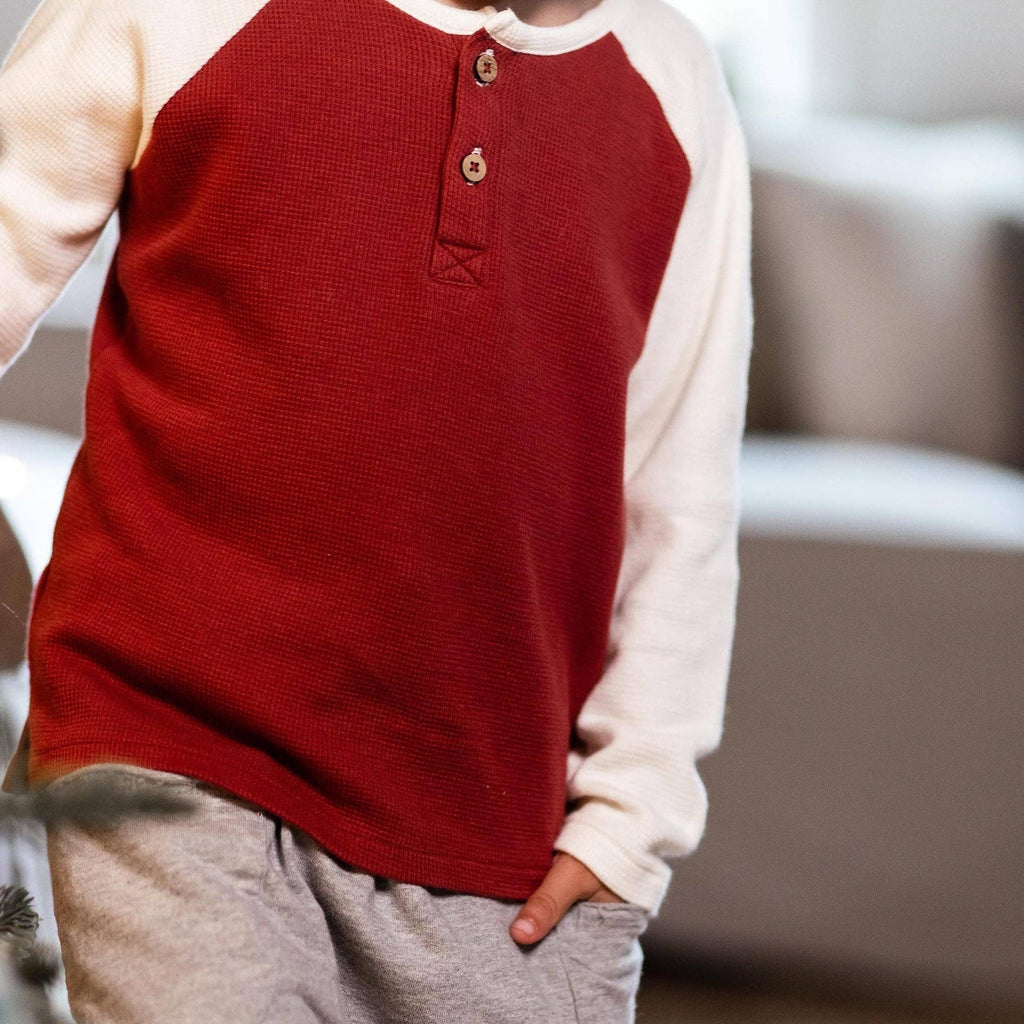 Close-up of a toddler wearing the Burt's Bees Baby - Thermal Organic Boy Tee & Pants Set - Brick Red, featuring a warm brick red thermal top with cream sleeves and soft gray pants, perfect for cozy everyday wear.