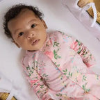 Baby wearing a pink floral outfit lying on a white surface