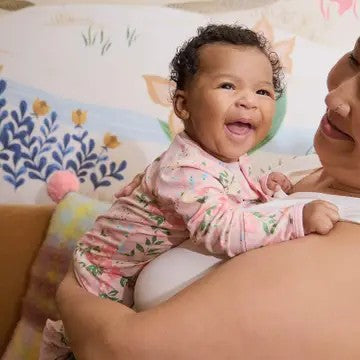 Baby in a floral onesie being held by an adult in a colorful room.