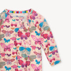 A close-up of a long-sleeve baby romper featuring a colorful butterfly print on a light beige base. The brand label 'eco-friendly clothes' is visible inside the collar.