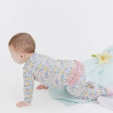 A baby crawling on a white studio floor wearing a long-sleeve footed onesie with a dense pastel floral print and a pink ruffled back detail.