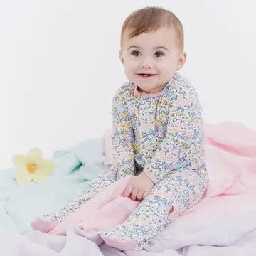 A baby sitting on pastel blankets wearing a long-sleeve footed pajama with a dense multicolor floral print.