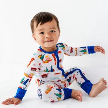 Toddler sitting and smiling wearing colorful pajamas with cityscape designs, styled to complement Convertible Footies - Bamboo - Blue Chicago, from a curated children’s boutique.