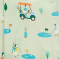A close-up of a light sage green fabric with a repeating cartoon golf course print. The pattern features stylized golf carts, players, golf balls, flags, and trees in muted teal, blue, yellow, and orange colors.
