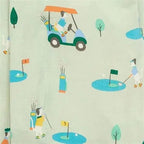 A close-up of a light sage green fabric with a repeating cartoon golf course print. The pattern features stylized golf carts, players, golf balls, flags, and trees in muted teal, blue, yellow, and orange colors.